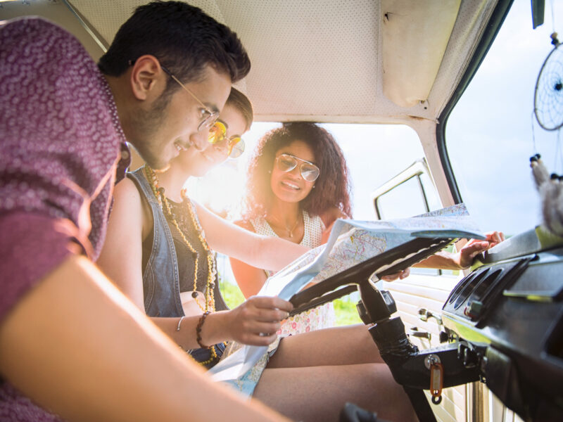 Mixed group of happy young people in a camper van looking at a road map